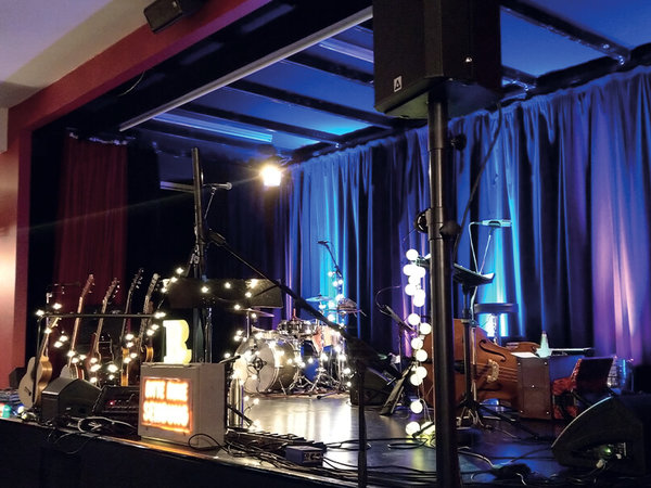 The stage of the "Red Hall" cultural venue in Braunschweig Castle. On the stage, instruments are ready for a concert. In the foreground is the P 261-AMT | Cine loudspeaker on a stand, equipped with an AMT tweeter unit from Mundorf.